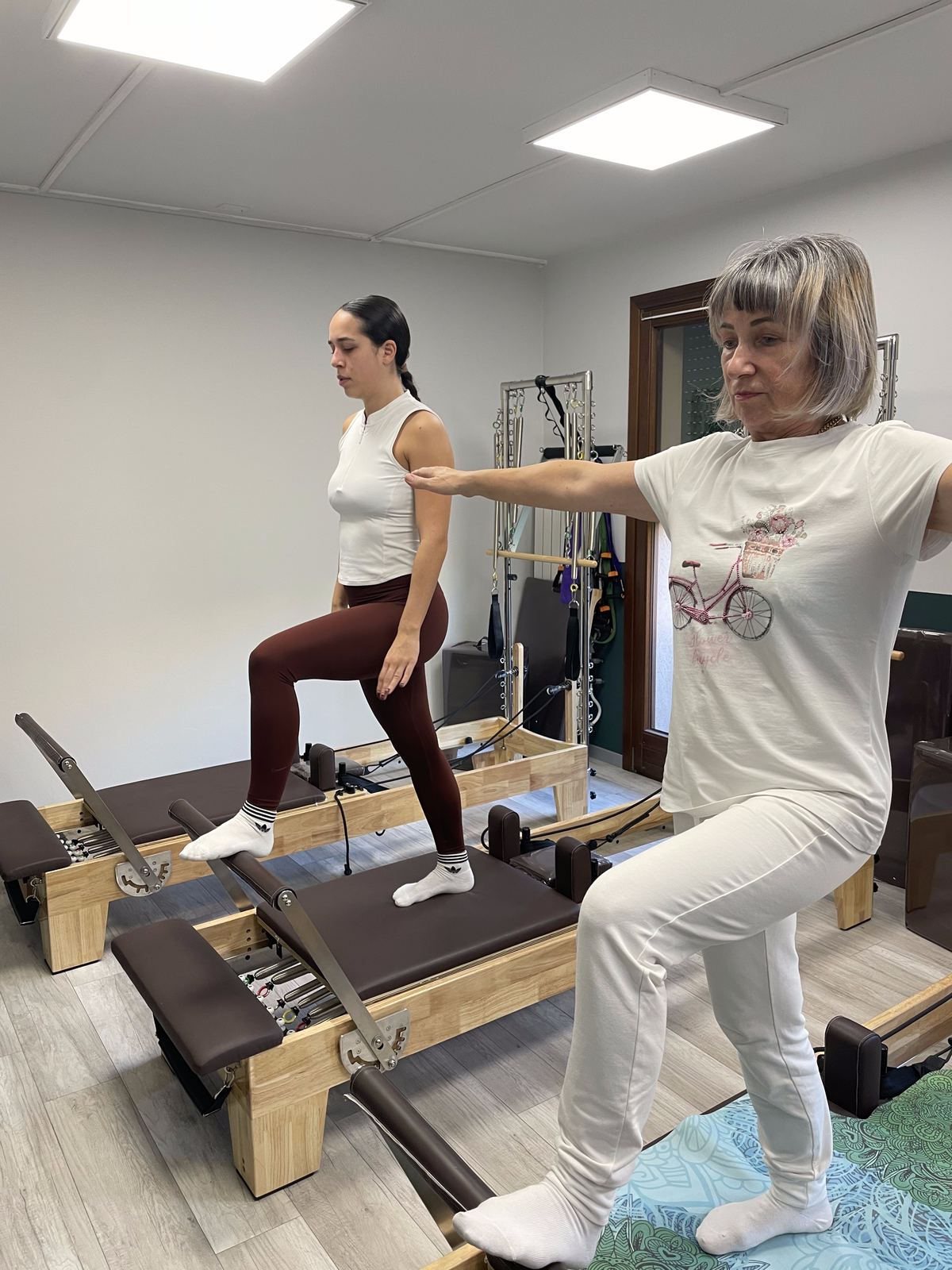 Due donne lavorano sul Reformer in studio con la gamba posteriore in estensione d'anca, il carrello che scorre indietro