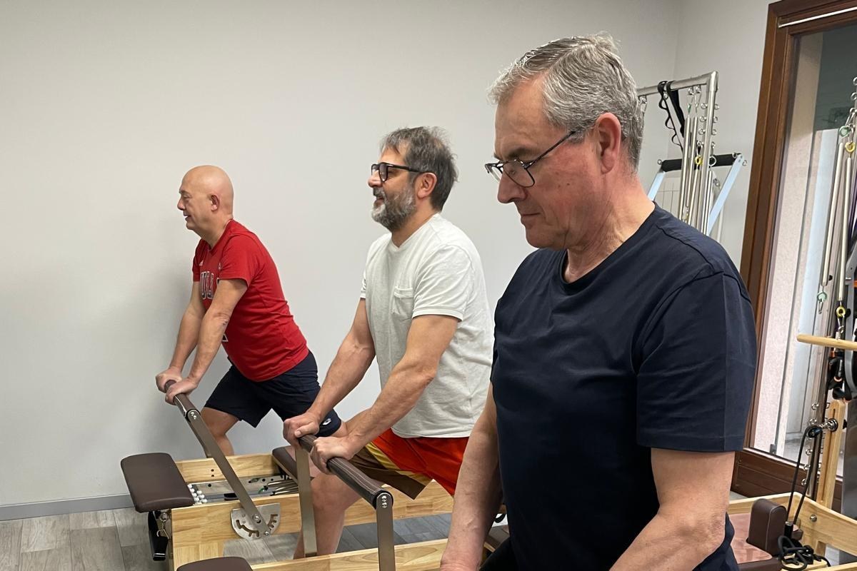 Tre uomini si allenano in piedi sul Reformer allo Studio Reformer di Monselice, con le mani sulla barra e lo sguardo in avanti